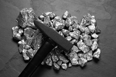 Photo of Pile of silver nuggets and hammer on black table, top view