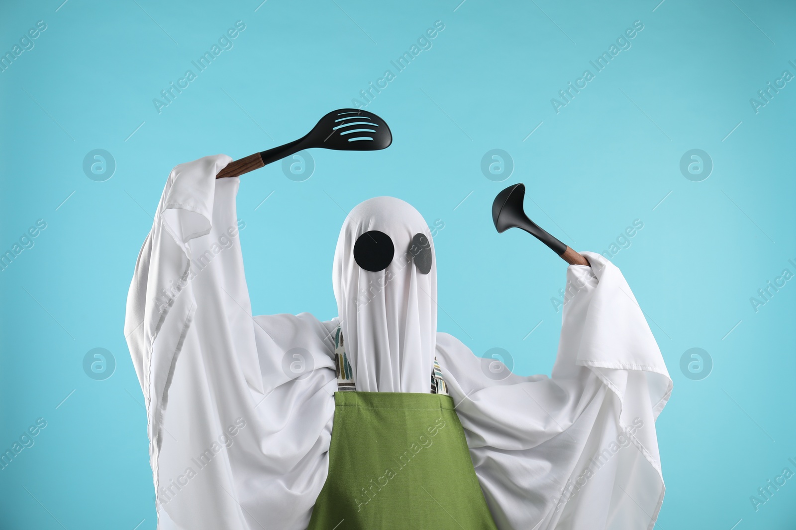 Photo of Woman in ghost costume and apron with kitchen set on light blue background