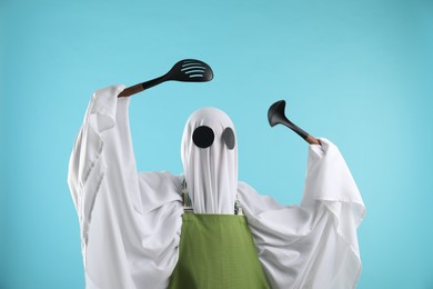 Photo of Woman in ghost costume and apron with kitchen set on light blue background