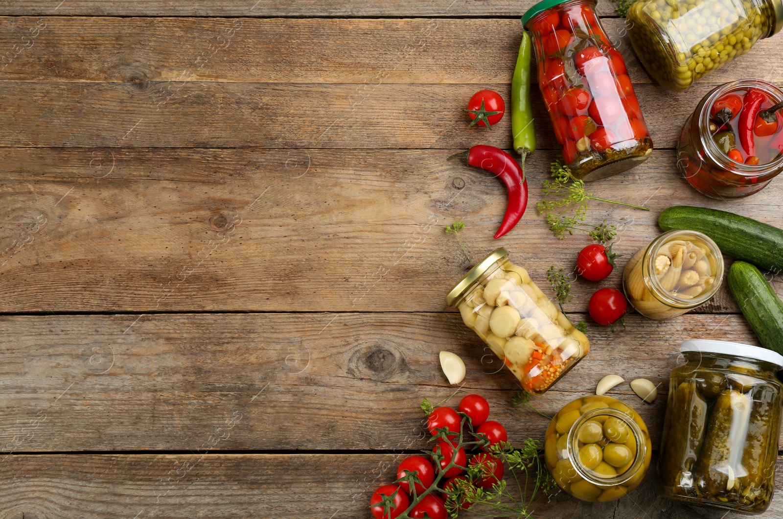 Photo of Jars of pickled vegetables and ingredients on wooden table, flat lay. Space for text