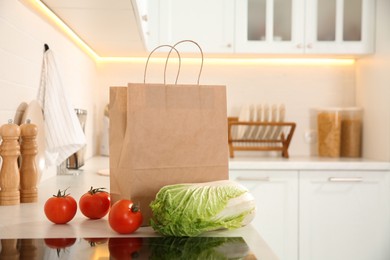 Photo of Paper shopping bag and fresh vegetables on white countertop in kitchen. Space for text