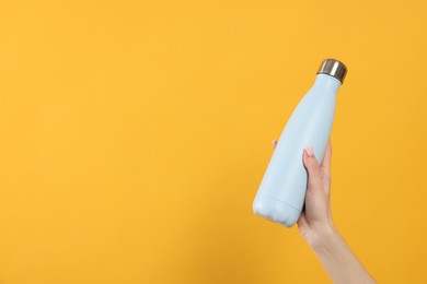 Photo of Woman holding thermos bottle on orange background, closeup. Space for text