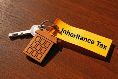 Photo of Inheritance Tax. Tag and key with key chain in shape of house on wooden table, closeup