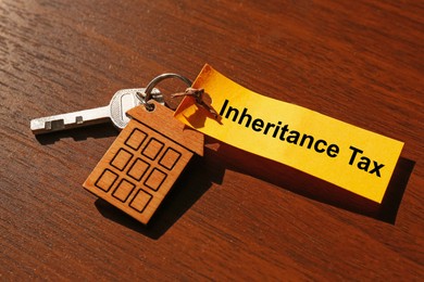 Inheritance Tax. Tag and key with key chain in shape of house on wooden table, closeup