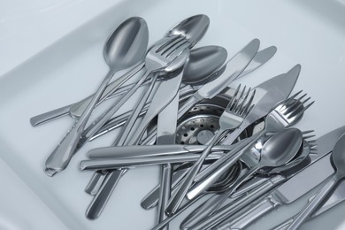 Photo of Washing silver spoons, forks and knives in kitchen sink with water, above view