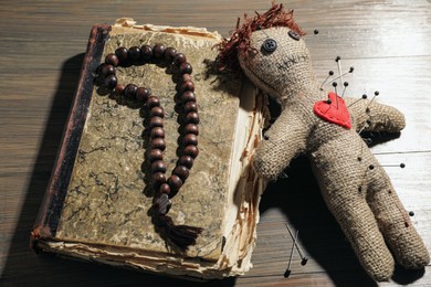 Photo of Voodoo doll with pins, old book and beads on wooden table