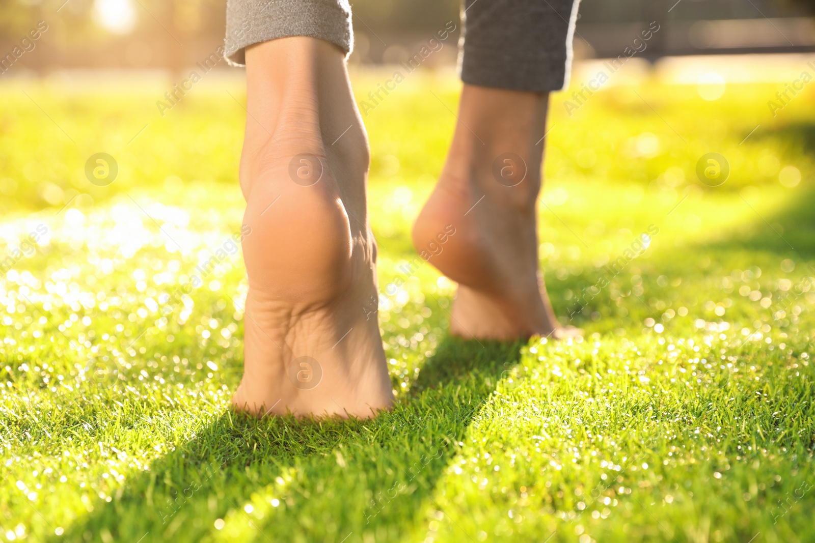 Photo of Young woman walking barefoot on fresh green grass, closeup