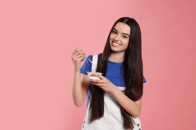 Photo of Happy teenage girl with delicious yogurt and spoon on pink background. Space for text