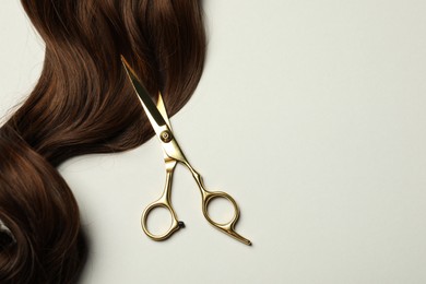 Professional hairdresser scissors with brown hair strand on light grey background, top view. Space for text