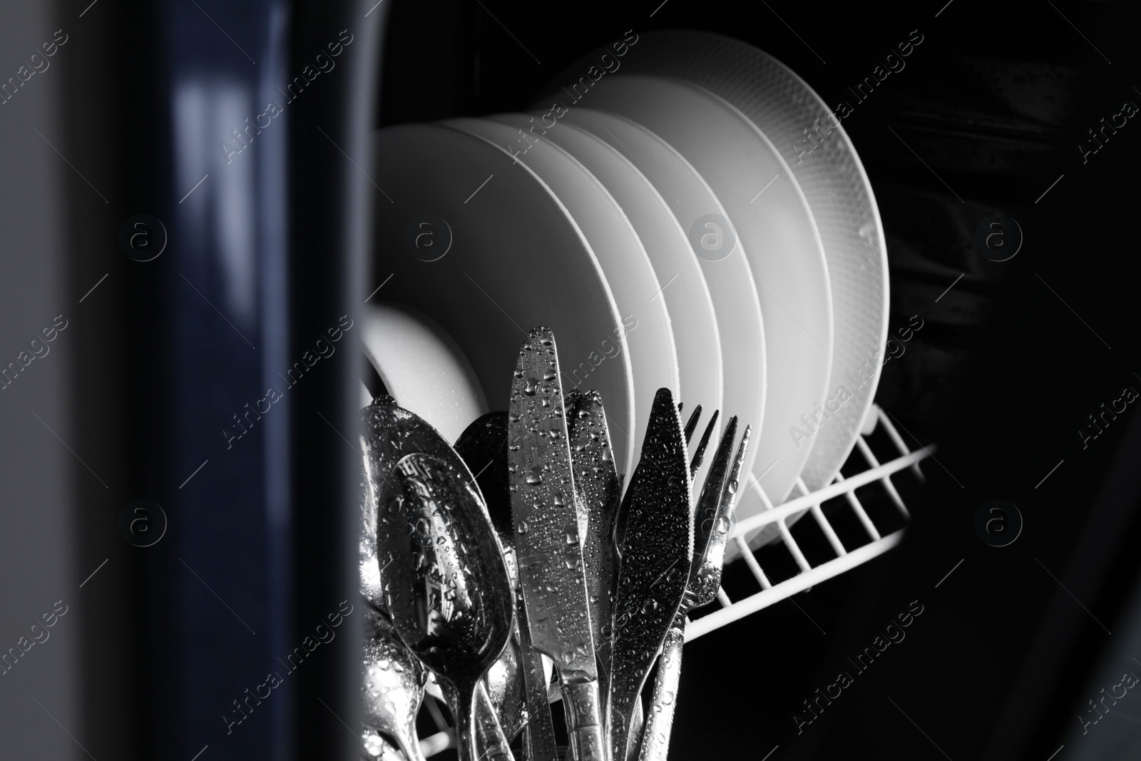 Photo of Clean plates and cutlery in dishwasher, closeup