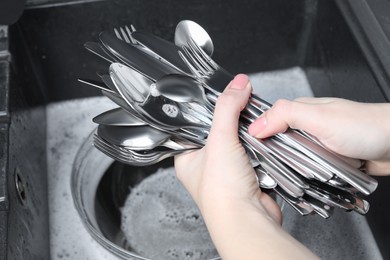 Woman holding clean silver kitchenware near sink, closeup