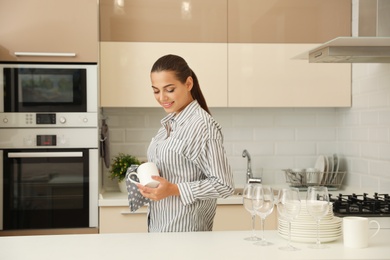 Photo of Young woman wiping clean cup in kitchen. Dish washing