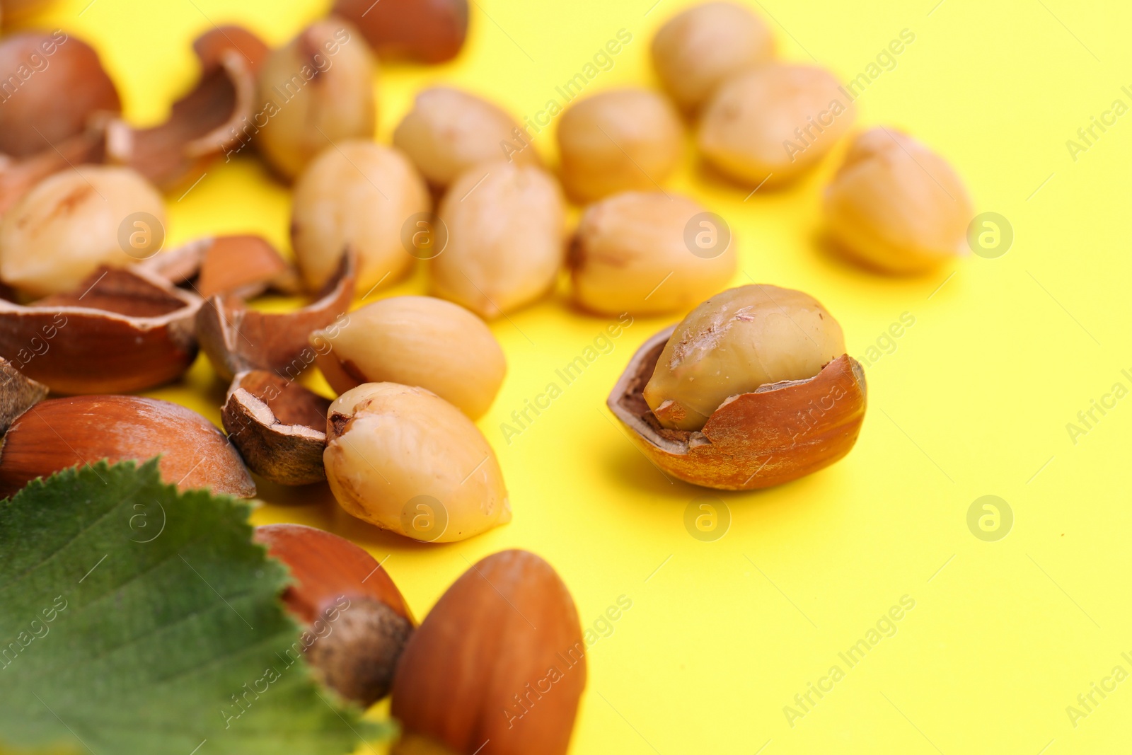 Photo of Tasty organic hazelnuts and leaves on yellow background, closeup