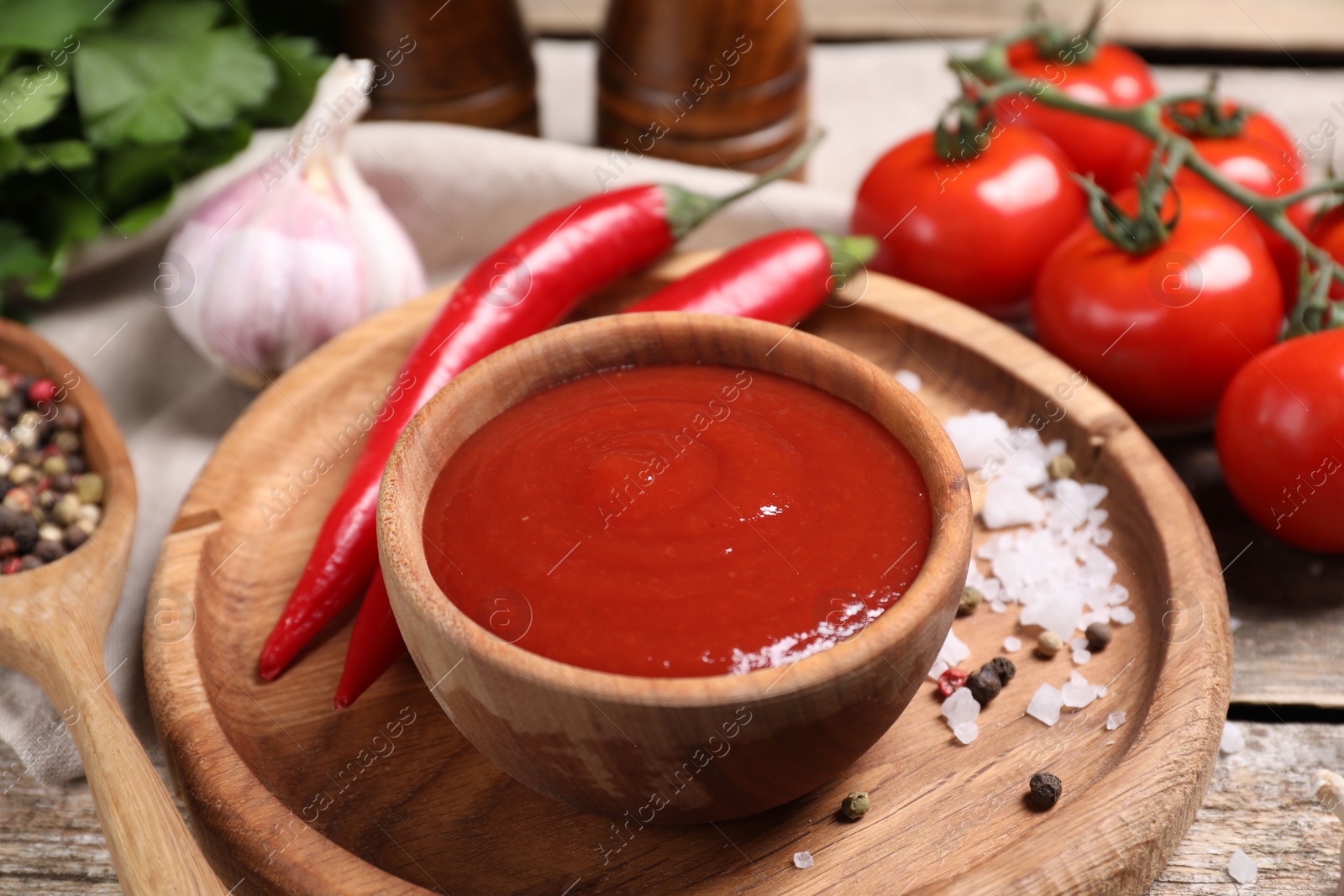 Photo of Delicious ketchup in bowl, chili pepper and spices on wooden table, closeup. Tomato sauce