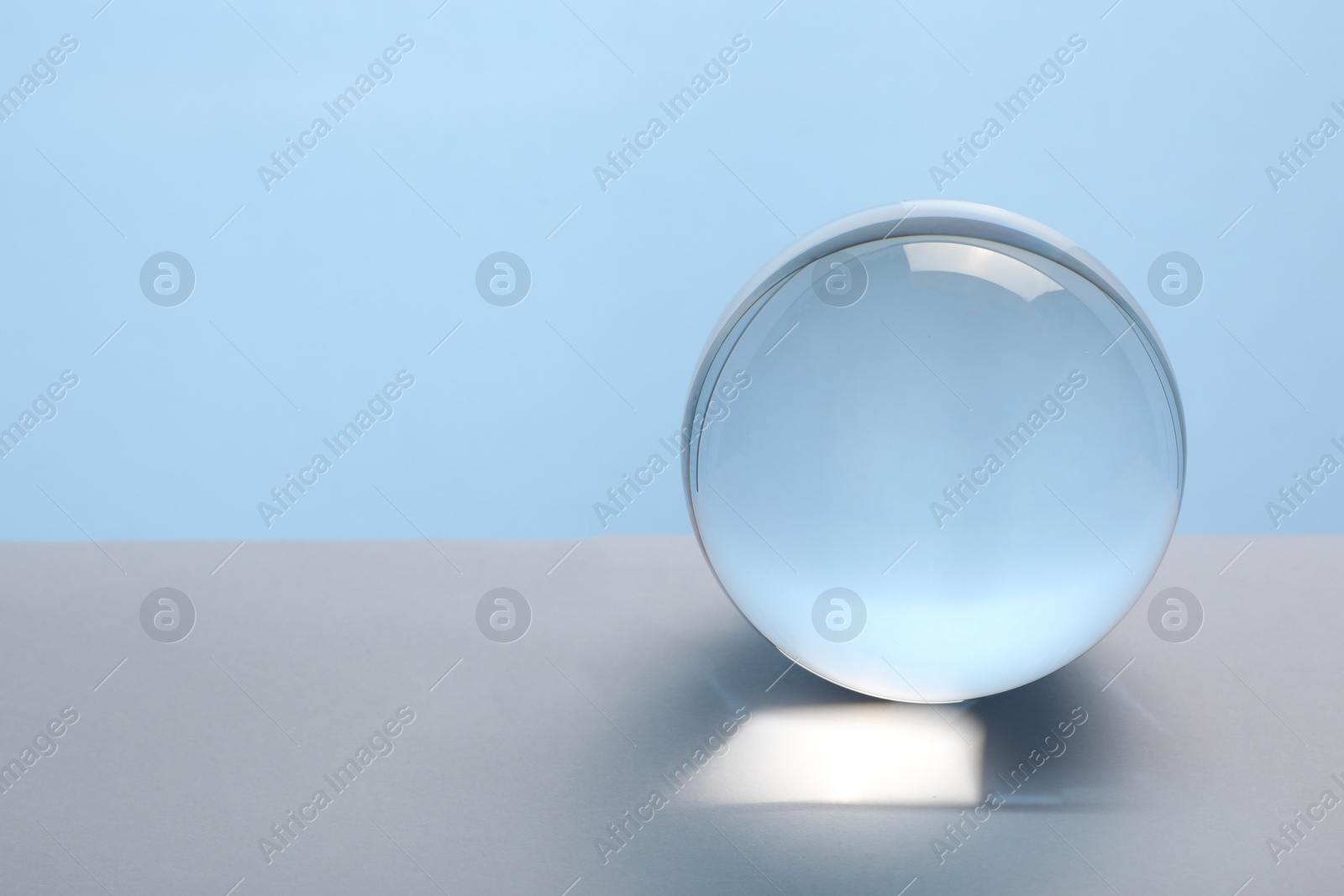 Photo of Transparent glass ball on table against light blue background. Space for text