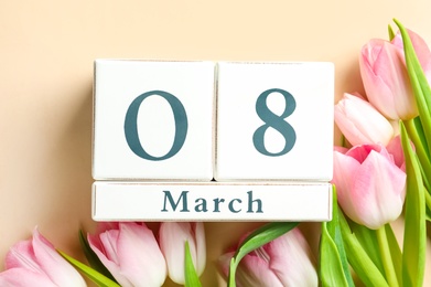 Wooden block calendar with date 8th of March and tulips on beige background, flat lay. International Women's Day