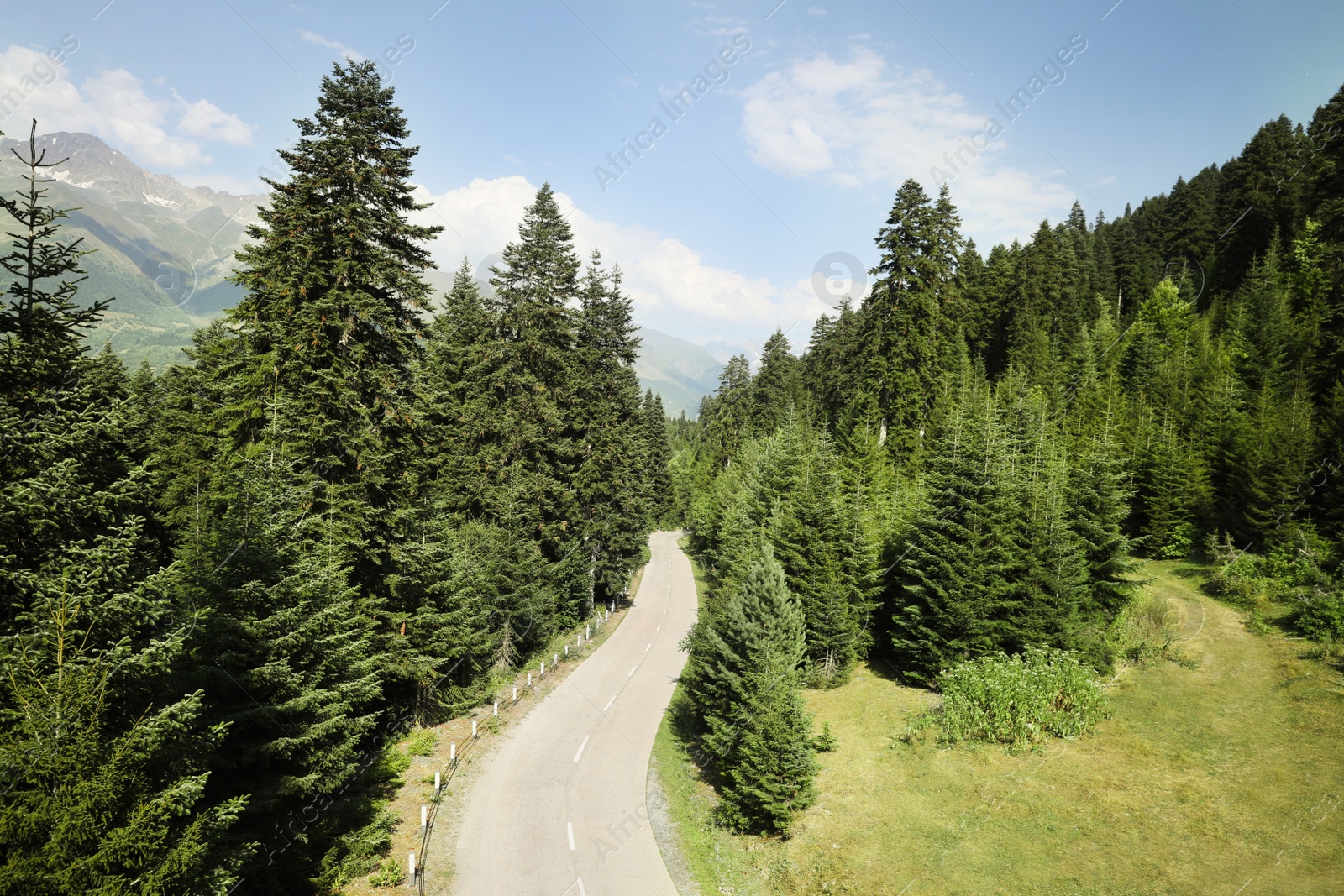 Photo of Beautiful road with trees near mountains under light blue cloudy sky