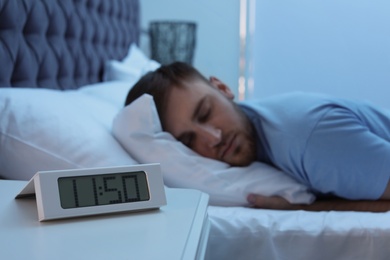 Alarm clock on table and young man sleeping in bed at night