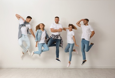 Group of young people in jeans jumping near light wall