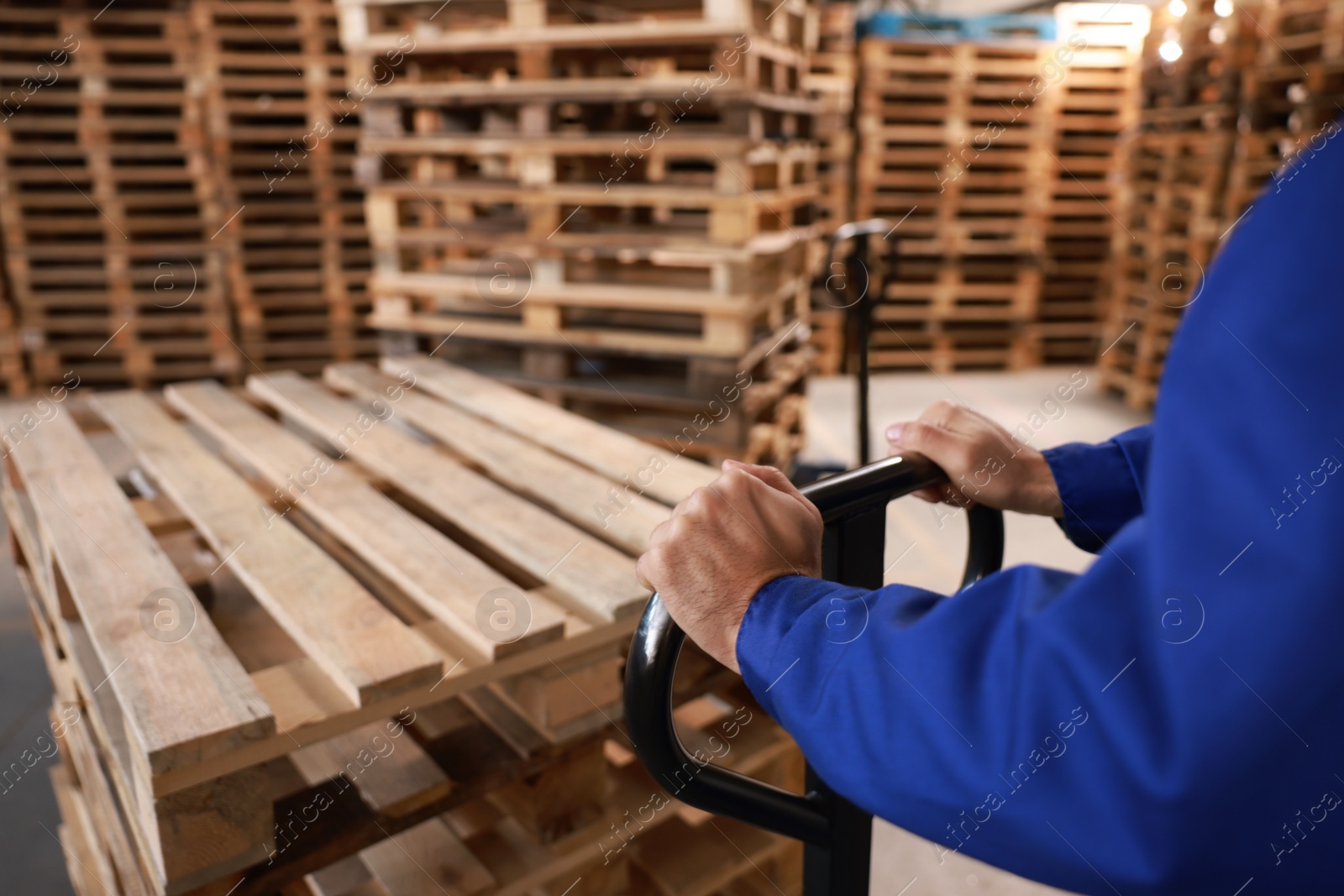 Image of Worker moving wooden pallets with manual forklift in warehouse, closeup