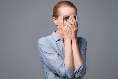 Young woman feeling fear on grey background