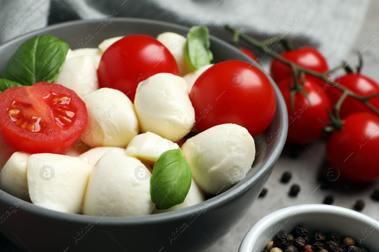 Photo of Delicious mozzarella balls in bowl, tomatoes and basil leaves on table, closeup