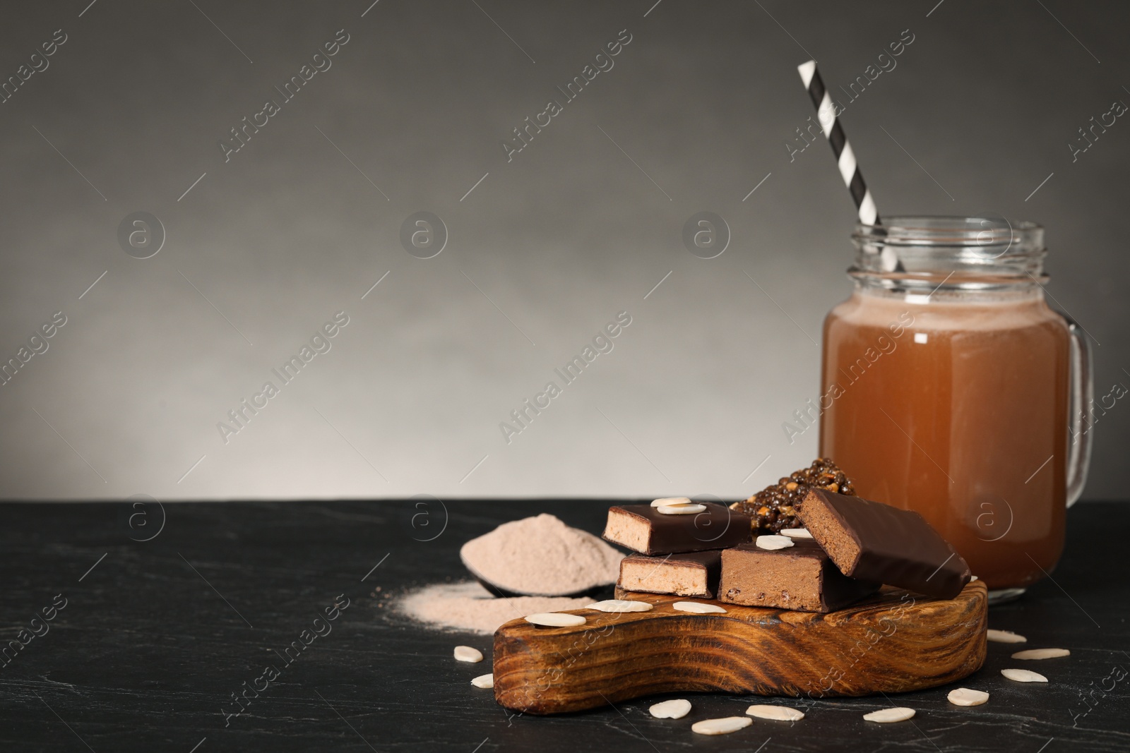 Photo of Different energy bars, almond flakes, protein cocktail and powder on black table. Space for text