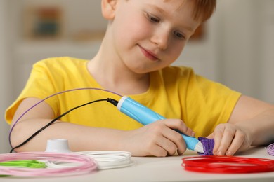 Photo of Boy drawing with stylish 3D pen at white table, selective focus