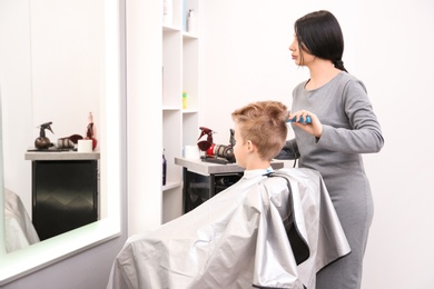 Photo of Professional female hairdresser working with little boy in salon