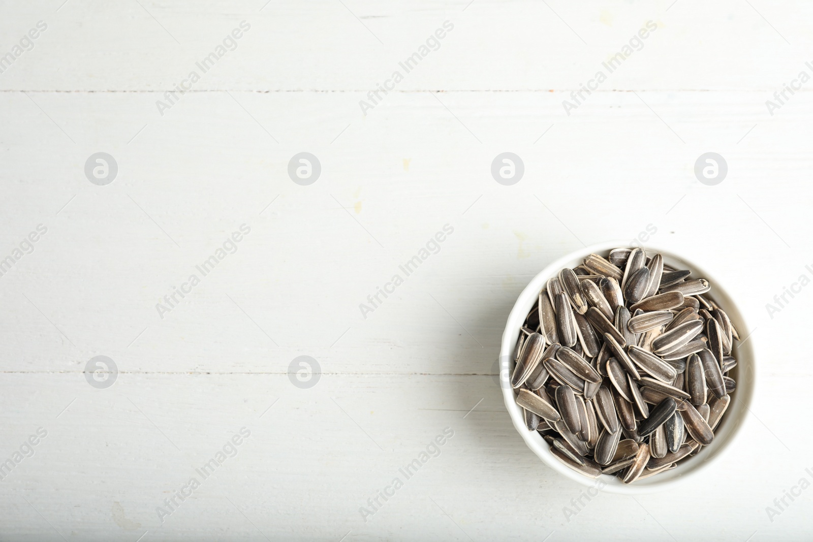 Photo of Organic sunflower seeds on white wooden table, top view. Space for text