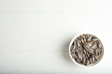 Photo of Organic sunflower seeds on white wooden table, top view. Space for text