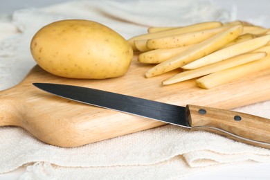 Photo of Whole and cut potatoes with knife on white towel, closeup. Cooking delicious french fries