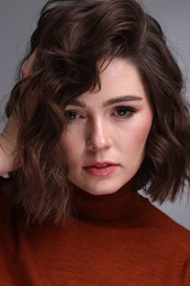 Portrait of beautiful young woman with wavy hairstyle on grey background