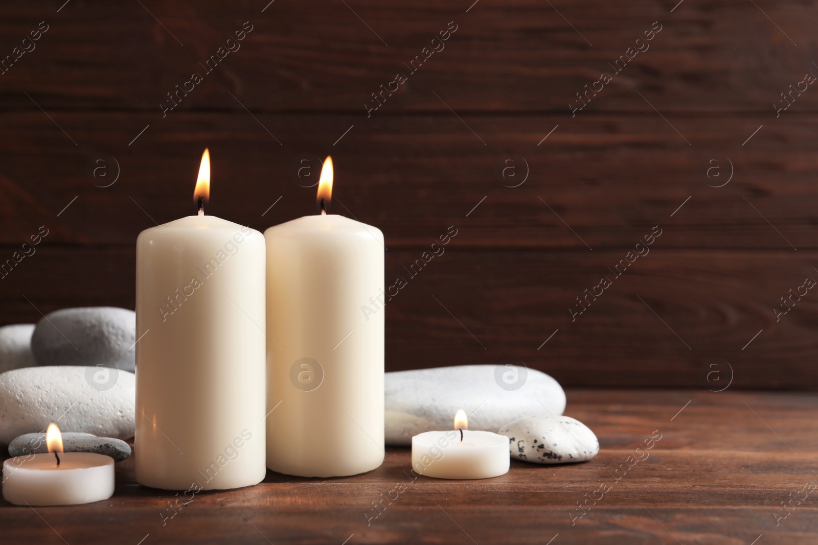 Photo of Beautiful composition with spa stones and burning candles on wooden table