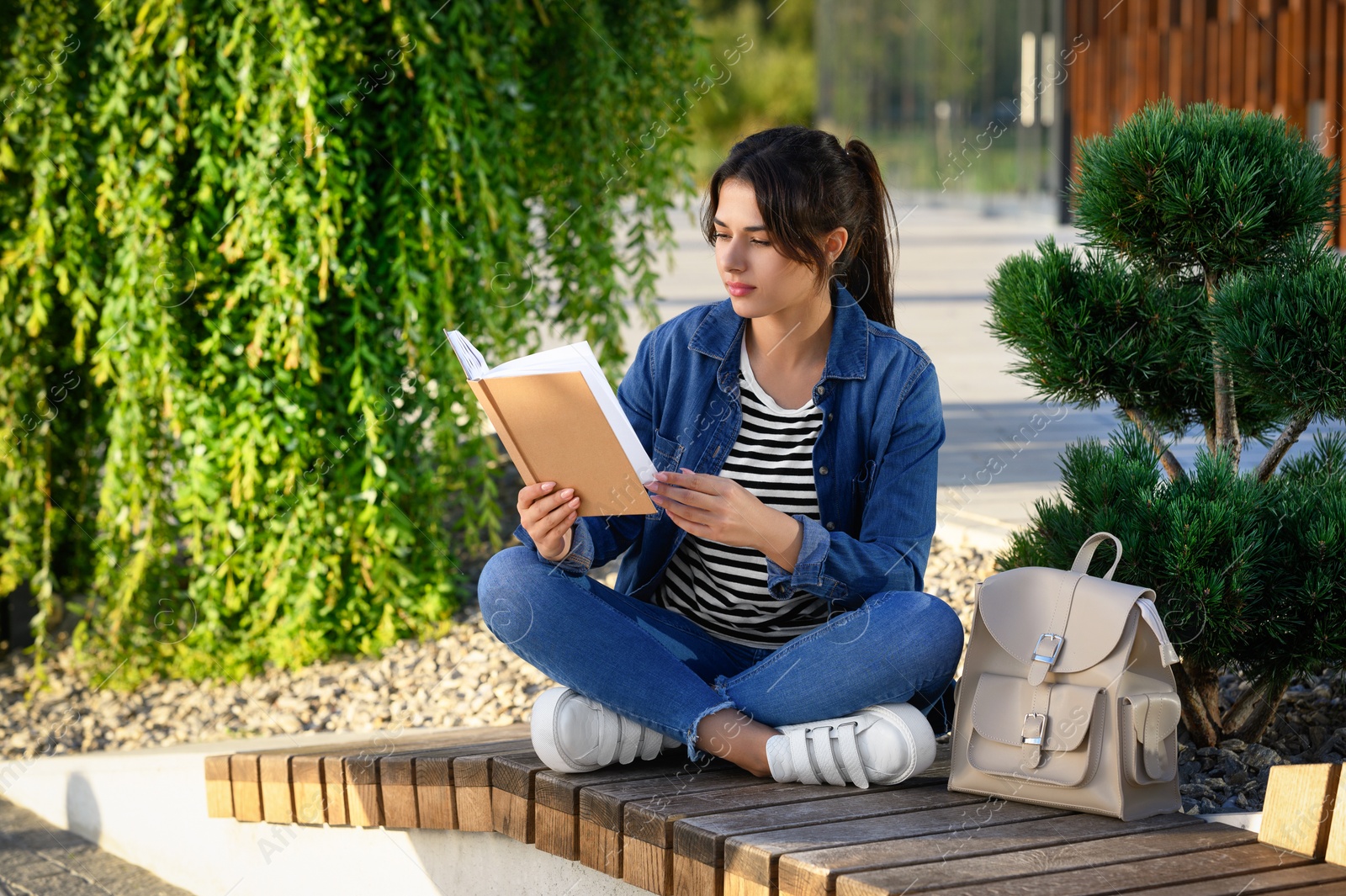 Photo of Young woman reading book on bench outdoors