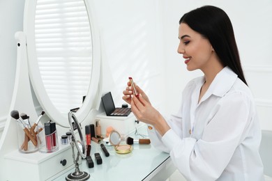 Beautiful woman applying makeup near mirror in room