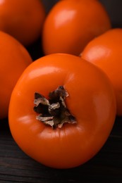 Photo of Delicious ripe persimmons on dark wooden table, closeup