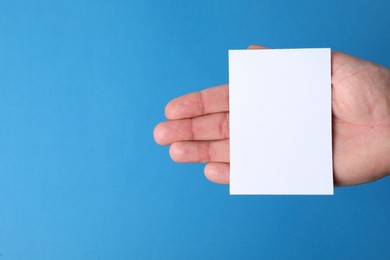 Photo of Man holding paper card on blue background, closeup. Mockup for design