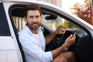 Happy bearded man with smartphone sitting in car