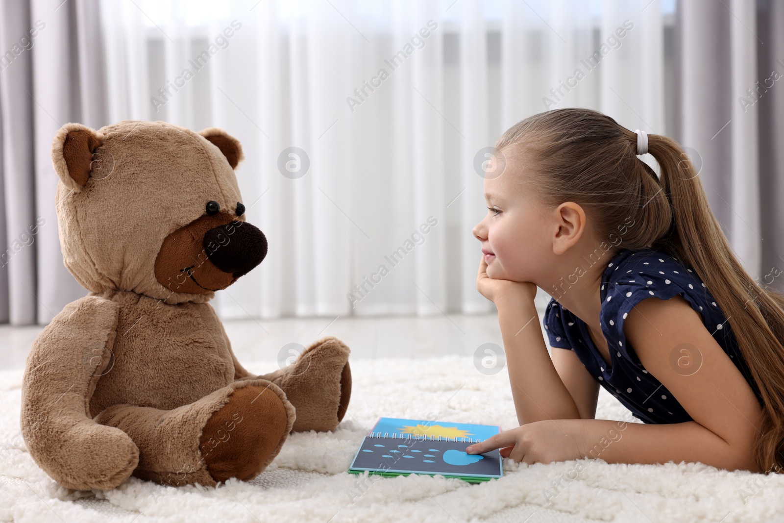 Photo of Cute little girl playing with teddy bear at home