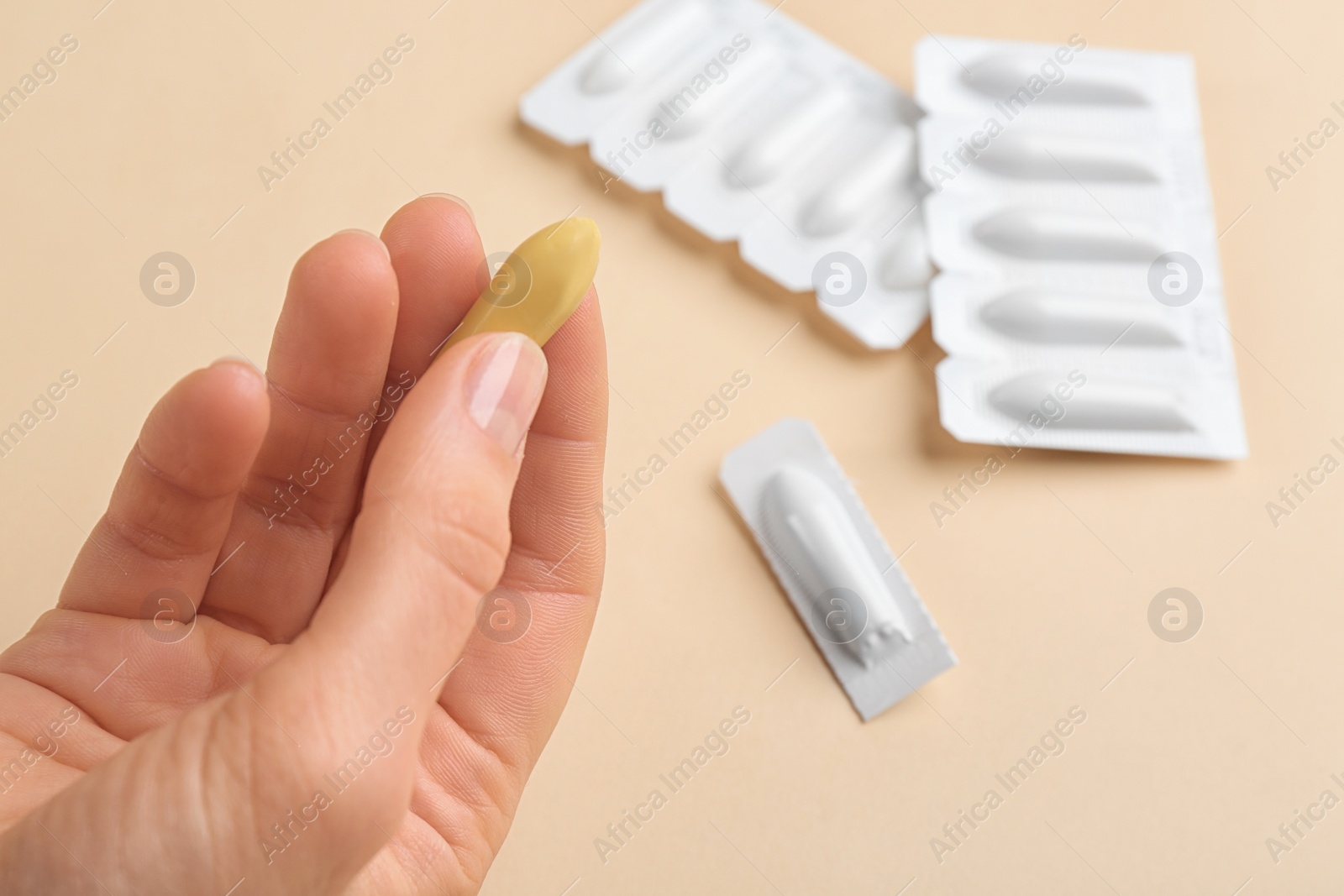 Photo of Woman holding unpacked suppository on beige background, closeup. Hemorrhoid treatment