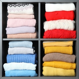 Many knitted winter clothes stacked on shelves near white background