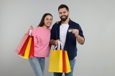 Happy couple with shopping bags and credit card on grey background