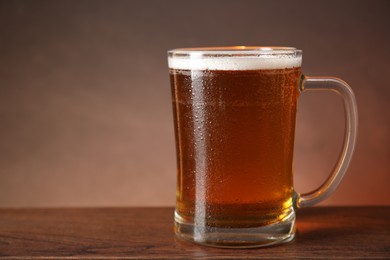 Mug with fresh beer on wooden table against brown background, closeup. Space for text