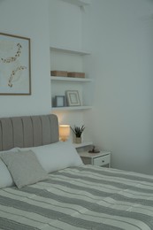 Photo of Large bed, pictures and shelves with accessories in stylish bedroom