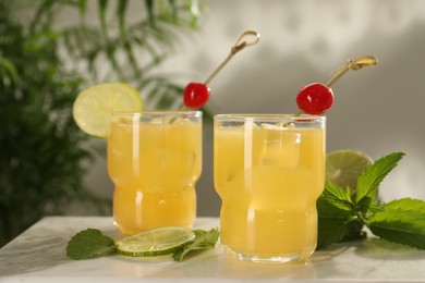 Photo of Glasses of tasty pineapple cocktail with cherry, lime and mint on white table
