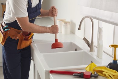 Photo of Plumber using plunger to unclog sink drain in kitchen, closeup