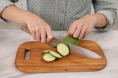 Photo of Cooking process. Woman cutting zucchini at white marble countertop, closeup