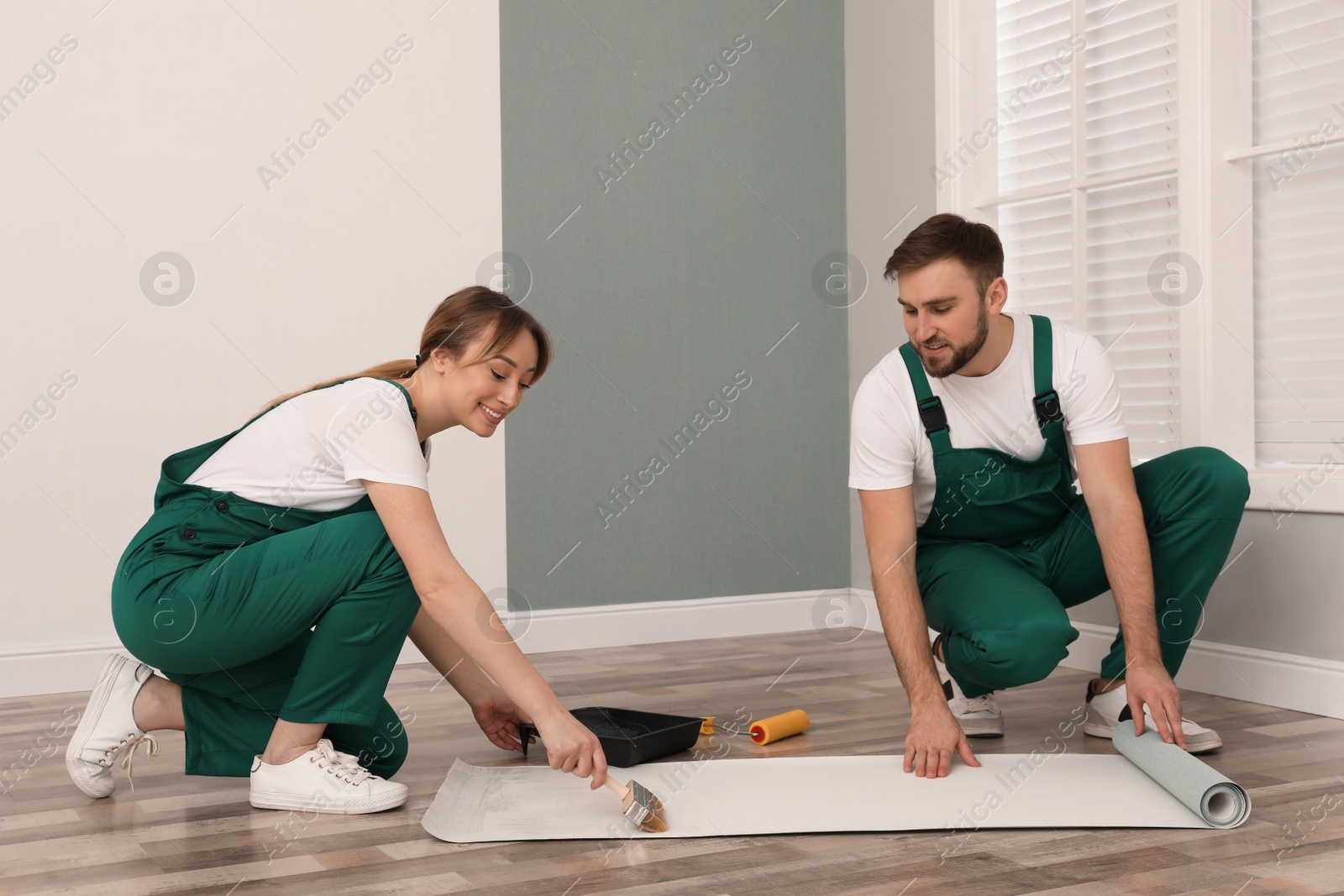 Photo of Workers applying glue onto wall paper sheet on floor indoors