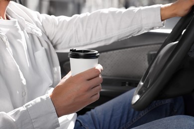Photo of Coffee to go. Man with paper cup of drink driving his car, closeup
